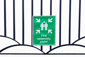 Fire assembly point sign at workplace car park fence wall