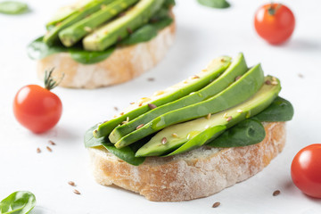 Two ciabatta toast with sliced avocado olive oil, spinach and flax and sesame seeds. Healthy vegetarian Breakfast on white background