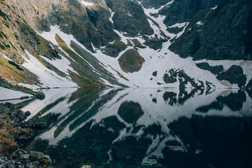 Mystical reflection of snow and mountains in water of Czarny Staw Black Pond, Tatra Mountains, Poland