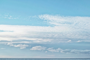 Cumulus and cirrocumulus clouds in the clear bright blue sky in the afternoon on the sea coast with a small strip of the sea below