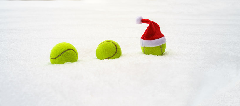 Santa hat on tennis ball on white snow winter background. Merry Christmas and New year concept with tennis balls. Close up, sport lifestyle, funny. Isolated