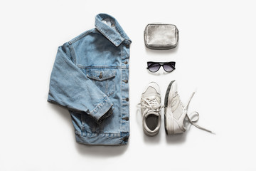 Casual fashion clothes and accessory set on white background. Jean jacket, sneakers, sunglasses, bag. Flat lay, top view.
