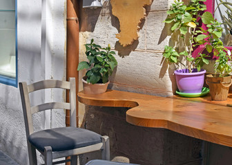 Gray chair next to the wooden tables on which there are pots with potted flowers. A cozy place on the street near the house, a cute corner with flowers