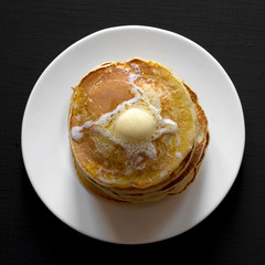 Homemade pancakes with butter on white plate over black background, overhead view. Flat lay, from above. Closeup.