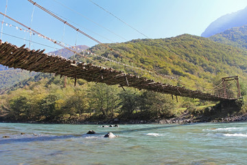 Long pedestrian suspension bridge over the mountain river Bzyb on a sunny autumn day in Abkhazia.