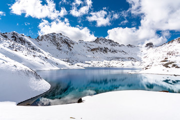 A clear blue alpine lake reflects the surrounding snowy mountains