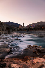 landscape of a medieval bridge over a turbulent river at sunset