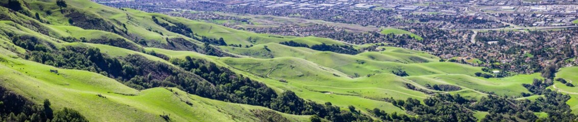 Aerial view of green hills at the base of Mission Peak in south San Francisco bay area, a popular area for hiking, residential areas of Fremont in the background, California