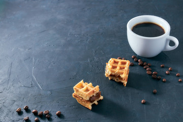 Homemade breakfast, stone black table. Viennese waffles, a cup of coffee, scattered coffee beans, vertical view, copy space