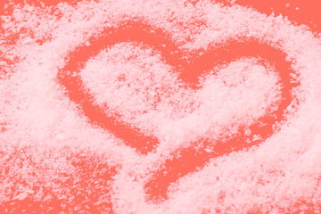 Heart drawn with snow on coral background.
