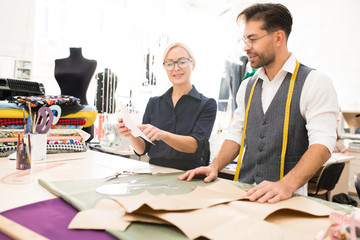Fototapeta premium Waist up portrait of two fashion designers working on clothes while standing at table in atelier workshop, copy space