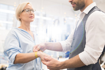 Fototapeta premium Portrait of unrecognizable tailor measuring wrist of female client while fitting clothes in traditional atelier studio lit by sunlight, copy space