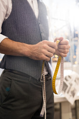 Mid section portrait of unrecognizable tailor holding measuring tape posing in traditional atelier studio