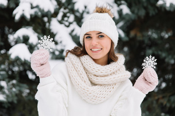 Happy woman in white winter clothes holding a beautiful snowflake in a park. Happy winter concept