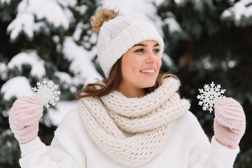 Happy woman in white winter clothes holding a beautiful snowflake in a park. Happy winter concept