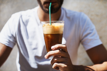 A man is drinking an ice coffee on a sunny day, taken from a front view