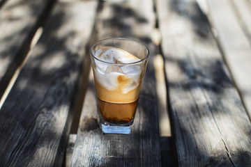 Iced coffee with milk and ice cubes on a wooden table