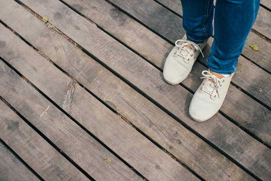 Girl in blue jeans and white sneakers standing on brown wooden floor. Copy space for the text.