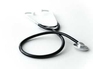 A doctors black flexible rubber and steel metal heart pulse stethoscope laying isolated on a white table top.