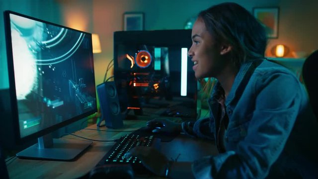 Beautiful and Excited Black Gamer Girl is Playing First-Person Shooter Online Video Game on Her Computer. Room and PC have Colorful Neon Led Lights. Cozy Evening at Home.