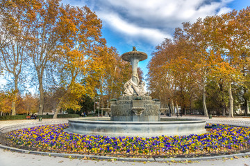 A water fountain with colorful trees around it at the Buen Retiro Park in Madrid in Chile