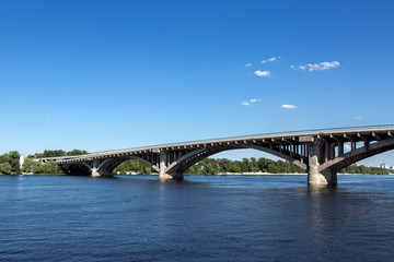 Concrete bridge arch structure across the river against the sky, bottom view of the road bridge.
