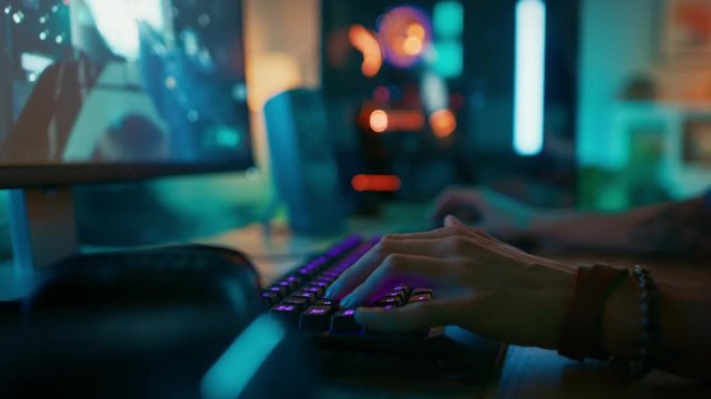 Close Up Hands Shot Showing a Gamer Pushing the Keyboard Buttons while Playing an Online Shooter Video Game. Keyboard Led Lights Change Color in Rainbow Spectrum. Gamer is Wearing a Bracelet. 