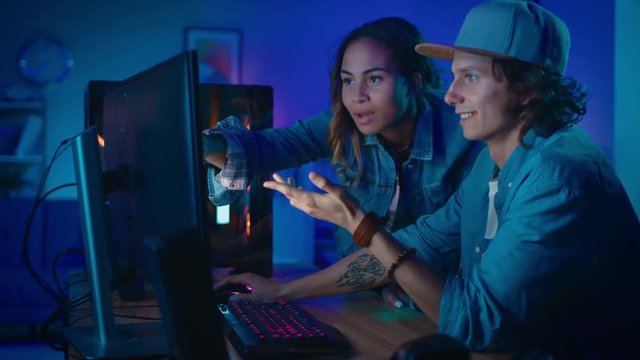 Pretty Black Girl Actively Talks and Explains Something to Her Friend and Points on a Computer Screen. Young Man Agrees with her Creative Ideas. Cozy Room is Lit with Warm and Neon Light.