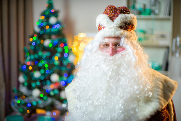 Portrait of Santa Claus in a red suit on the background of the Christmas tree.