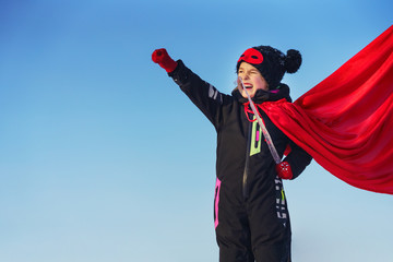 Funny little girl playing power super hero over blue sky background. Superhero concept.