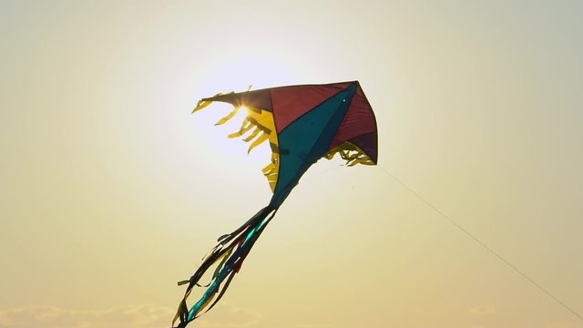 Close up toy kite flying high air in the wind against gold sunset sky background sun lens flare. Colorful kite flying in sunny summer sky. Toy children fun leisure activity recreation happy holiday