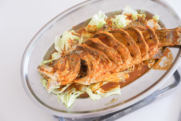 Thai dinner food fried barramundi fish with herb on the white plate over white table in restaurant