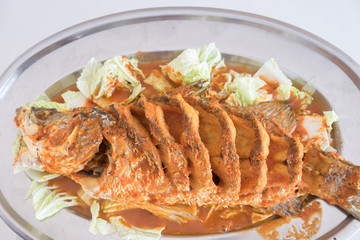 Thai dinner food fried barramundi fish with herb on the white plate over white table in restaurant