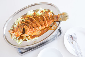 Thai dinner food fried barramundi fish with herb on the white plate over white table in restaurant