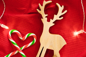 Christmas decoration. Wood Deer play toy and Candy over red background with light. Candy cane. 