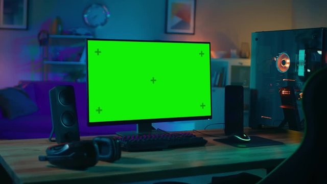 Powerful Personal Computer Gamer Rig with Mock Up Green Screen Monitor Stands on the Table at Home. Cozy Room with Modern Design is Lit with Warm and Neon Light.