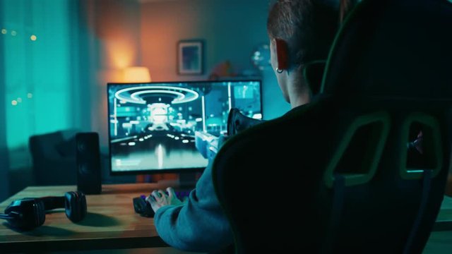 Back Shot of a Gamer Playing First-Person Shooter Online Video Game on His Powerful Personal Computer. Room and PC have Colorful Neon Led Lights. Cozy Evening at Home.