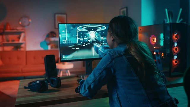 Back Shot of a Gamer Girl Playing First-Person Shooter Online Video Game on Her Powerful Personal Computer. Room and PC have Colorful Warm Neon Led Lights. Cozy Evening at Home.