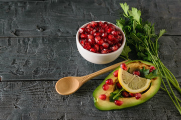 A bunch of parsley, a white bowl with pomegranate seeds and half avocado on the village table.
