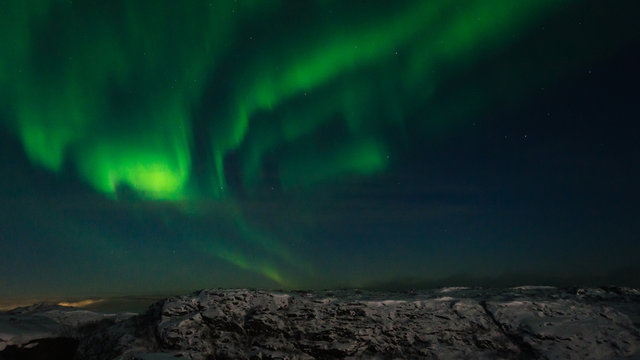 Beautiful northern lights, aurora in the night sky over the snow-covered hills.