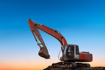 Excavator in construction site on sunset sky background