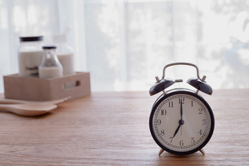 wood table with glass of milk and retro alarm clock in living room.