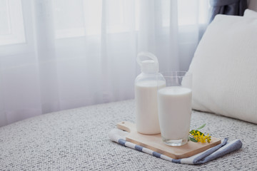 Obraz na płótnie Canvas A bottle of milk and glass of milk on bed in living room with white curtain windows background.