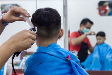 Little Asian boy and black hair age 4 years old getting haircut with red shirt barber man for prepare back to school on white background