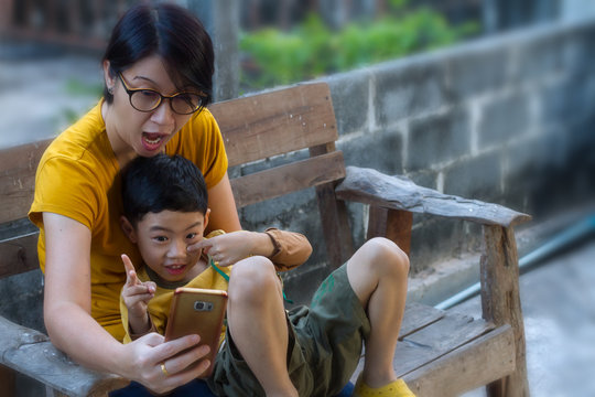 Mom And Son Selfie With Mobile Phone Background. Asian Black Hair 40s Woman And 4 Years Old Boy Happiness To Using Smart Phone Taking Photos With Sunset Effect. Selective Focus And Copy Space