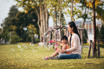 Happy Asian mother and daughter blowing bubbles in park outdoors