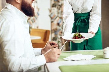 Girl waiter serves his dish in restaurant to a man