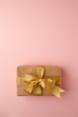Gift box with golden ribbon on pink pastel background with space. Minimal cincept of holiday. Top view