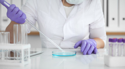 Close-up of professional female scientist in protective eyeglasses making experiment with reagents in laboratory. Medicine and research concept