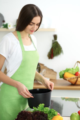 Beautiful Hispanic woman cooking soup in kitchen. Healthy meal and householding concepts